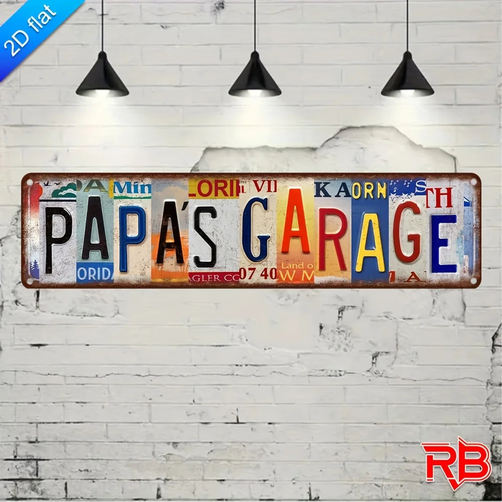 Vintage aluminum metal wall art sign with the text PAPA'S GARAGE painted on a white brick wall.
