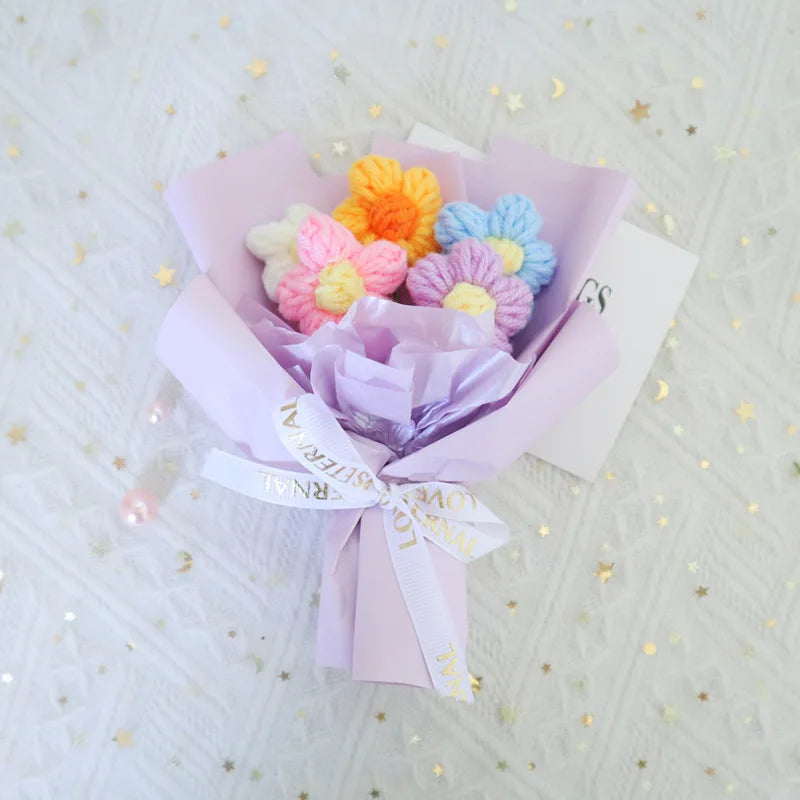 A handmade crochet sunflower mini bouquet in shades of orange, pink, and blue, wrapped in purple paper.