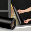 A hand is pulling a roll of black privacy window film across a window pane.