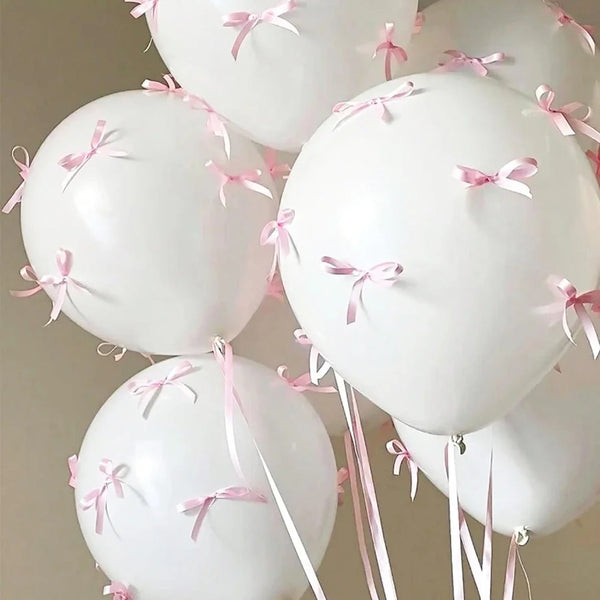 Un grupo de globos de látex blancos atados con cintas rosas.