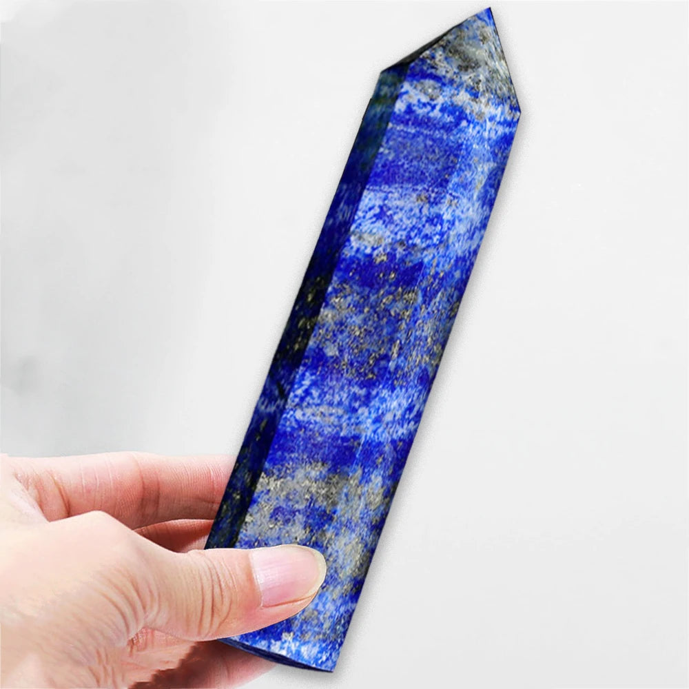 A hand holds a polished blue lapis lazuli crystal tower with shimmering gold inclusions.