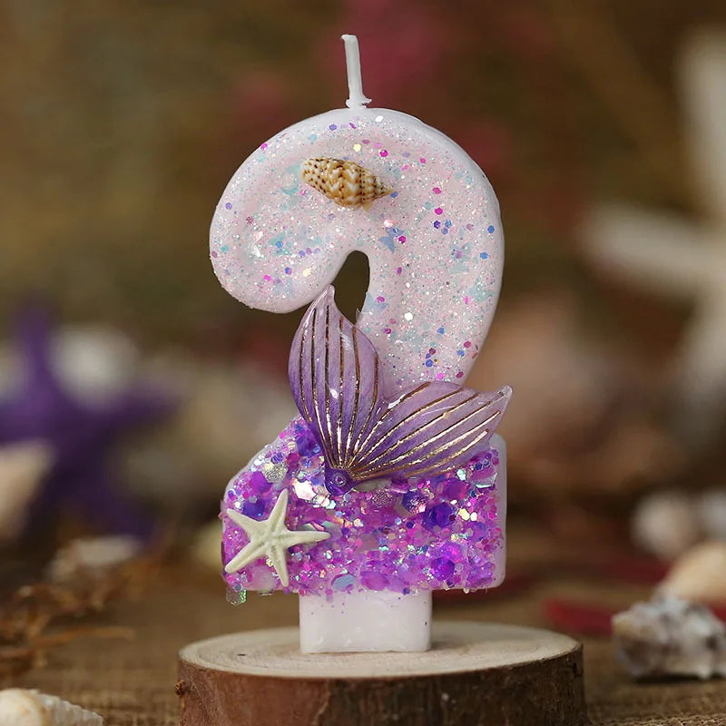 A pink birthday candle shaped like the number 9 decorated with glitter and a purple mermaid tail design.