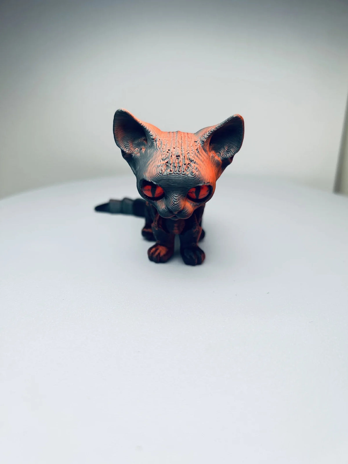 An orange and black articulated 3D printed figurine of a Siamese cat with intense red eyes.