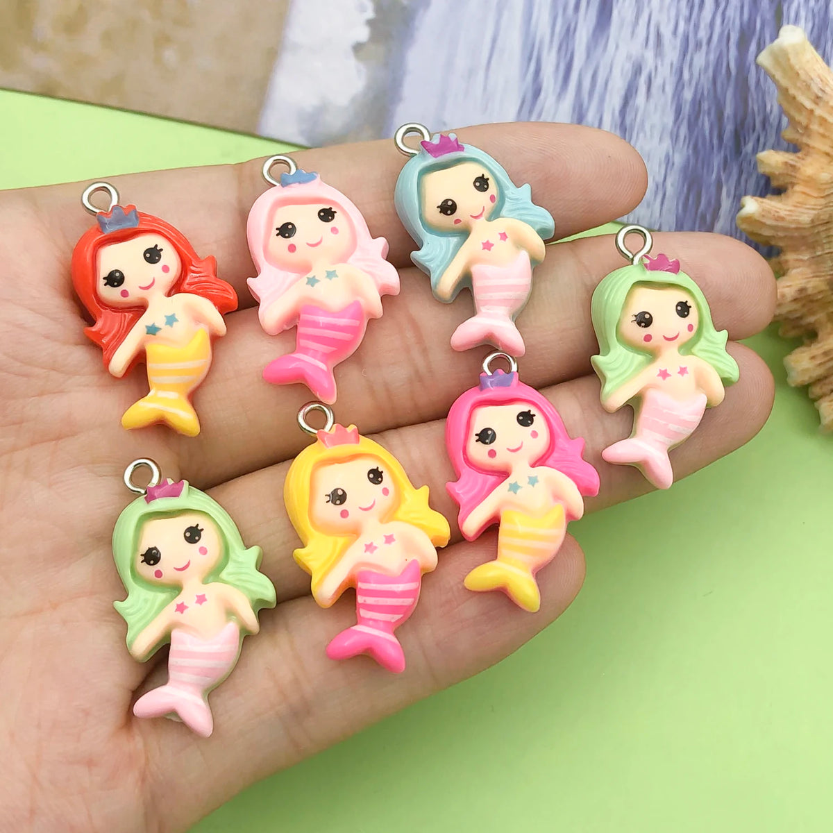 A hand holds several colorful resin mermaid princess charms for jewelry making