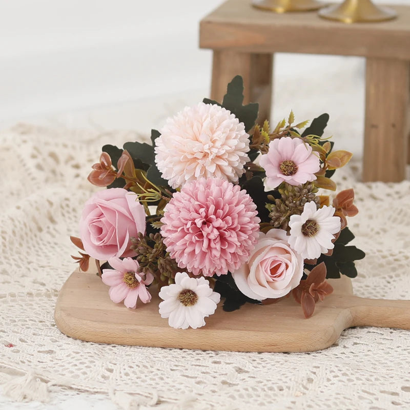A bouquet of pink and white silk flowers including roses and hydrangeas arranged on a wooden board.