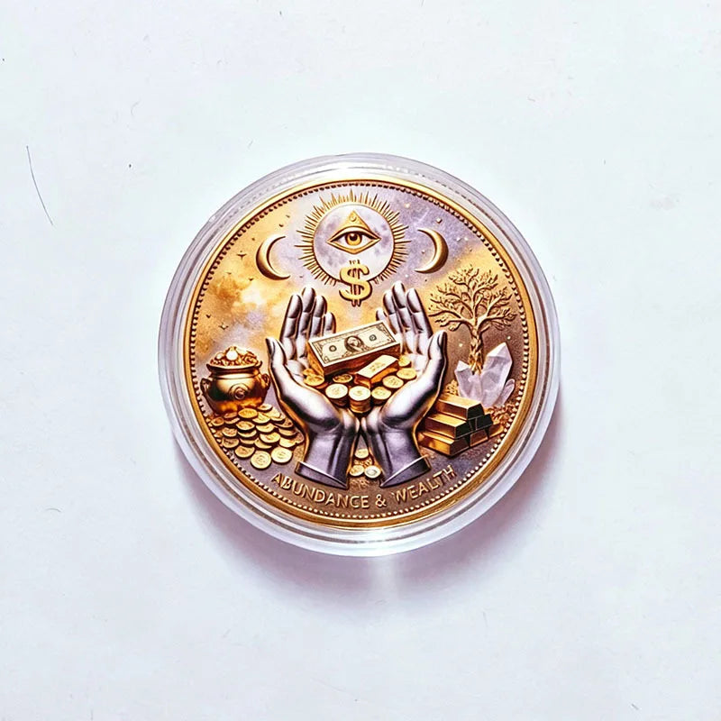 A round gold commemorative coin featuring an eye symbol, hands holding coins and a tree, labeled abundance and wealth.