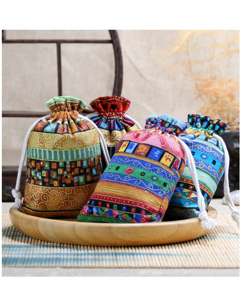 A set of ten vintage cotton drawstring gift pouches in various colorful patterns displayed on a wooden tray.