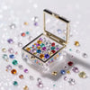 An open clear acrylic box filled with colorful diamond gemstones scattered on a white surface.