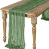 A sage green semi-sheer gauze table runner draped over a wooden table.