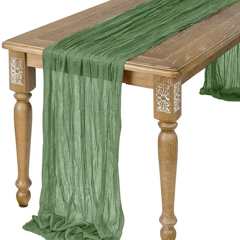 A sage green semi-sheer gauze table runner draped over a wooden table.
