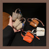 A hand holds a tan mini house handbag with a colorful wrist strap against a dark background.