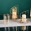 A set of elegant gold metal and glass candle holders with a white candle displayed on a dark surface.