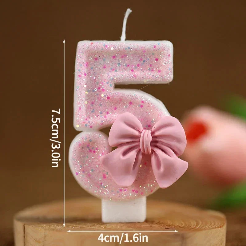 A pink glitter number cake candle set showing the number 5 and a pink bow on a wooden surface.