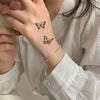 A close-up of a hand with black butterfly temporary tattoos on the wrist, set against a white shirt.