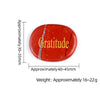 A reddish-orange oval crystal with a natural fracture, engraved with the word Gratitude.