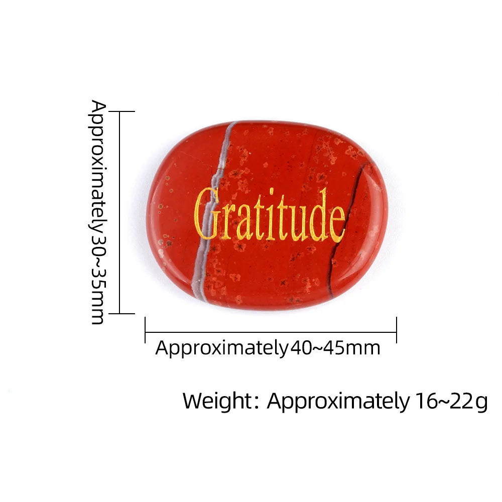 A reddish-orange oval crystal with a natural fracture, engraved with the word Gratitude.
