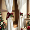 Festive Christmas curtain tie-backs with red bows and pinecones hanging in a wooden window frame.