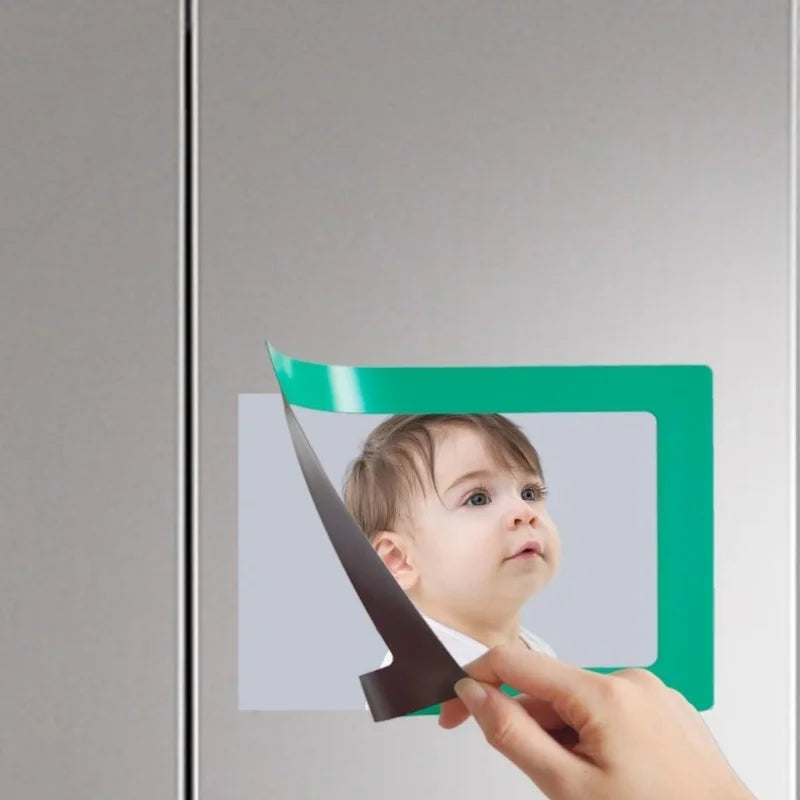 A hand is placing a magnetic photo frame onto a refrigerator door, showing the green frame and a child's face.