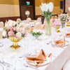A close-up of a gold trumpet vase filled with white flowers used as a wedding centerpiece.