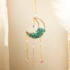 A gold moon-shaped crystal suncatcher with teal crystals and dangling prisms.