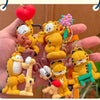 A hand holds several yellow Garfield cartoon character keychains and pendants.