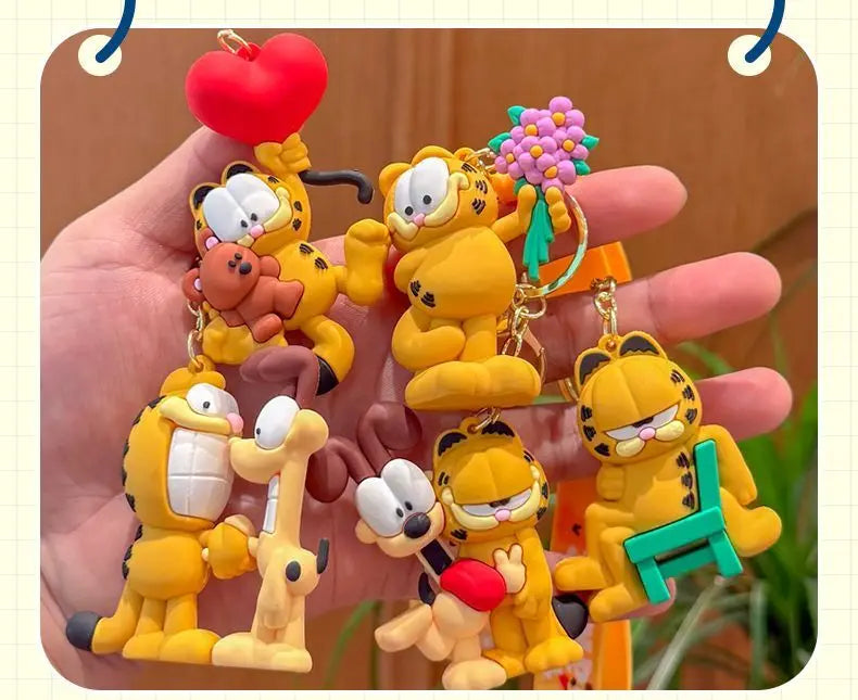 A hand holds several yellow Garfield cartoon character keychains and pendants.