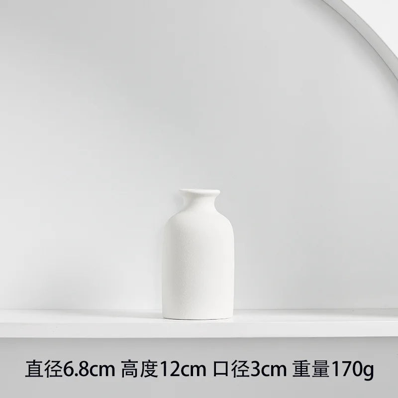 A white ceramic tabletop vase with a smooth, rounded shape is displayed on a white shelf.