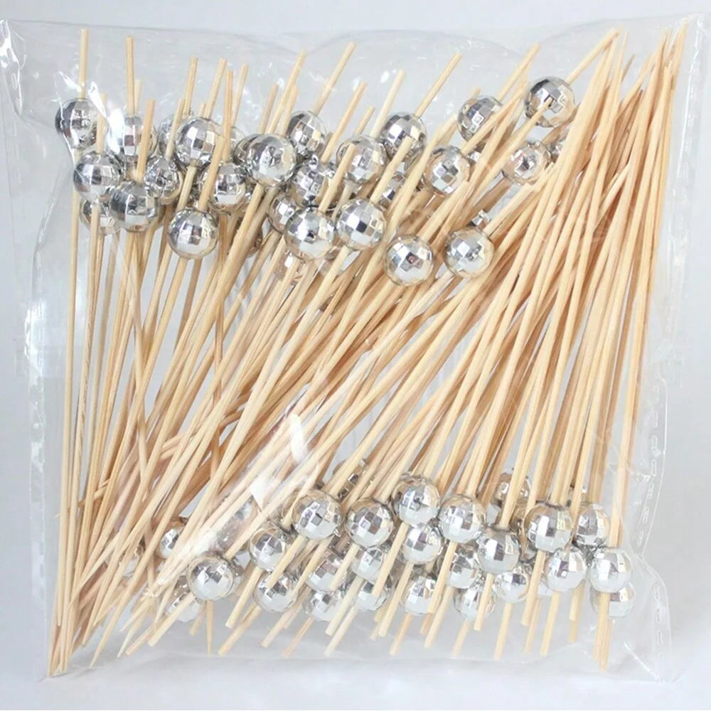 A bundle of bamboo fruit skewers with silver-colored spherical tops packaged in clear plastic.