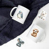 A white mug features watercolor illustrations of a blue bird and a white puppy on a dark gray fabric background.