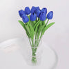 A bouquet of vibrant blue artificial tulip flowers in a clear glass vase on a white surface.