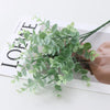 Green artificial fern and leaf sprigs arranged on a white surface.