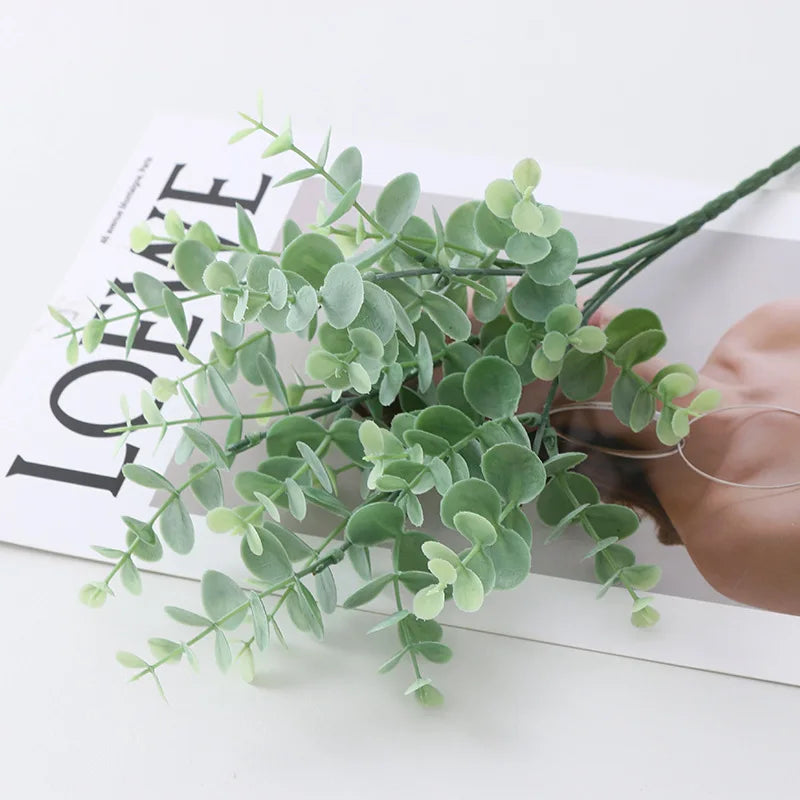 Green artificial fern and leaf sprigs arranged on a white surface.