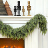 A green pine vine wreath decorated with antique brass and black figurines hangs over a white fireplace mantel.