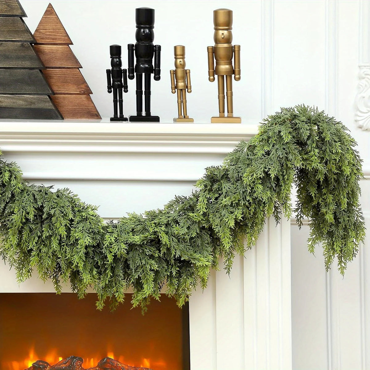 A green pine vine wreath decorated with antique brass and black figurines hangs over a white fireplace mantel.