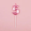 A pink number five candle with a thin white stick against a light pink background.