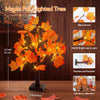 A lighted maple tree decoration with orange leaves displayed on a wooden surface.