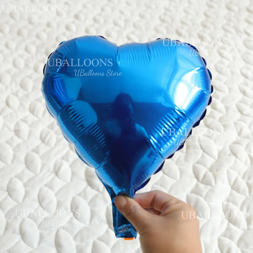 A hand holds a bright blue heart-shaped foil balloon against a white textured background.