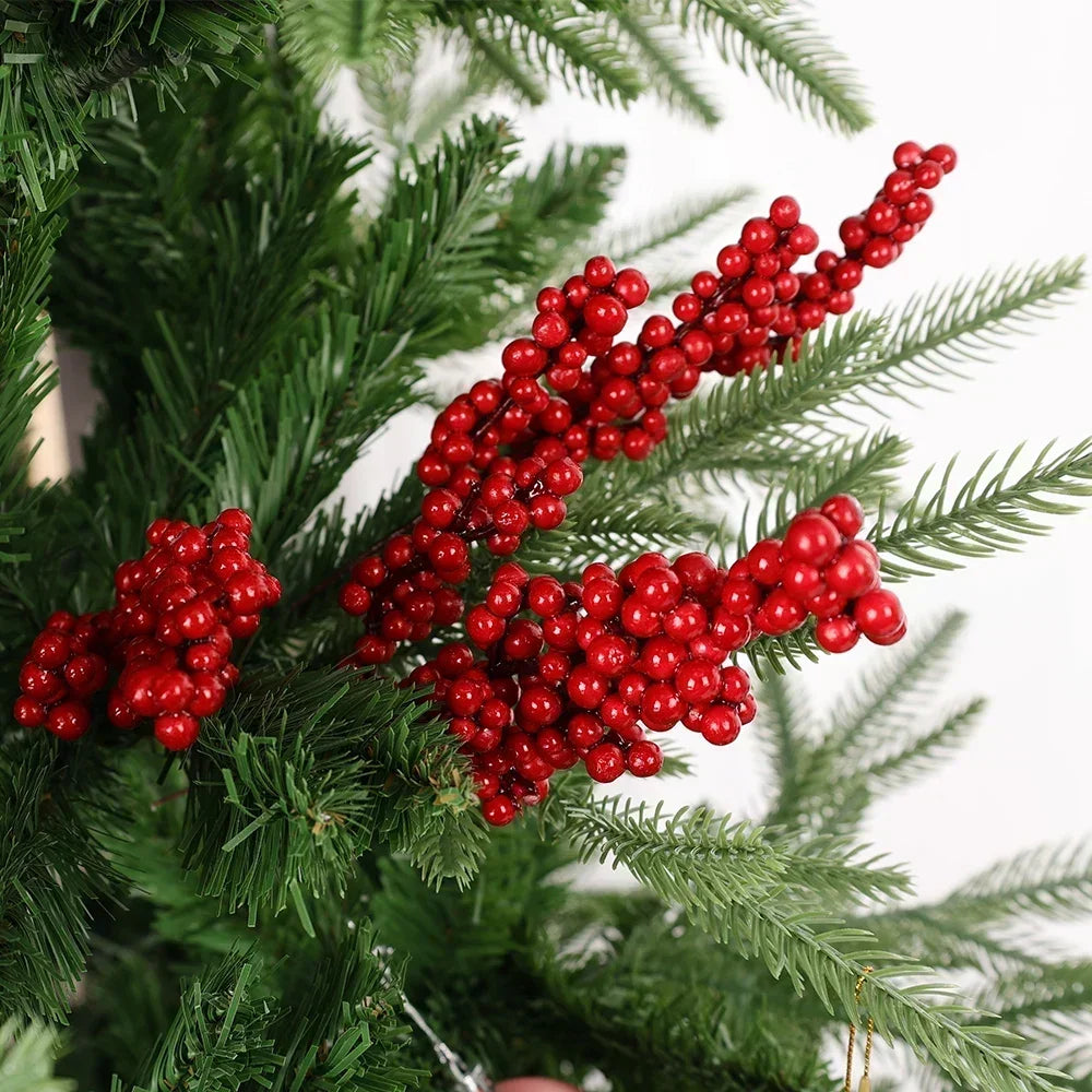 A branch of artificial green pine needles decorated with clusters of bright red holly berries for Christmas decor.