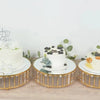 A set of three white cake stands decorated with fresh berries and greenery on a wooden surface.