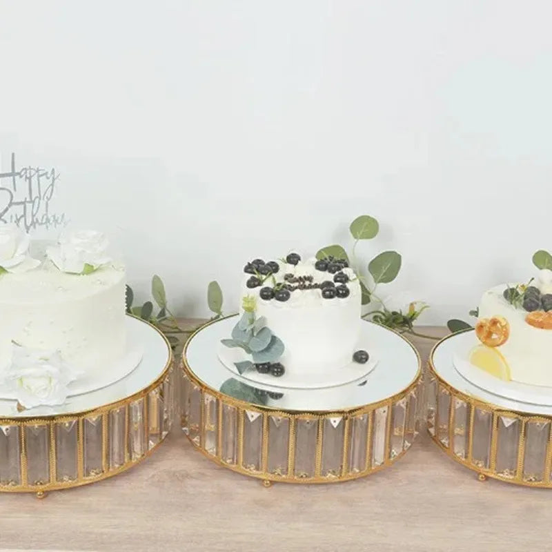 A set of three white cake stands decorated with fresh berries and greenery on a wooden surface.