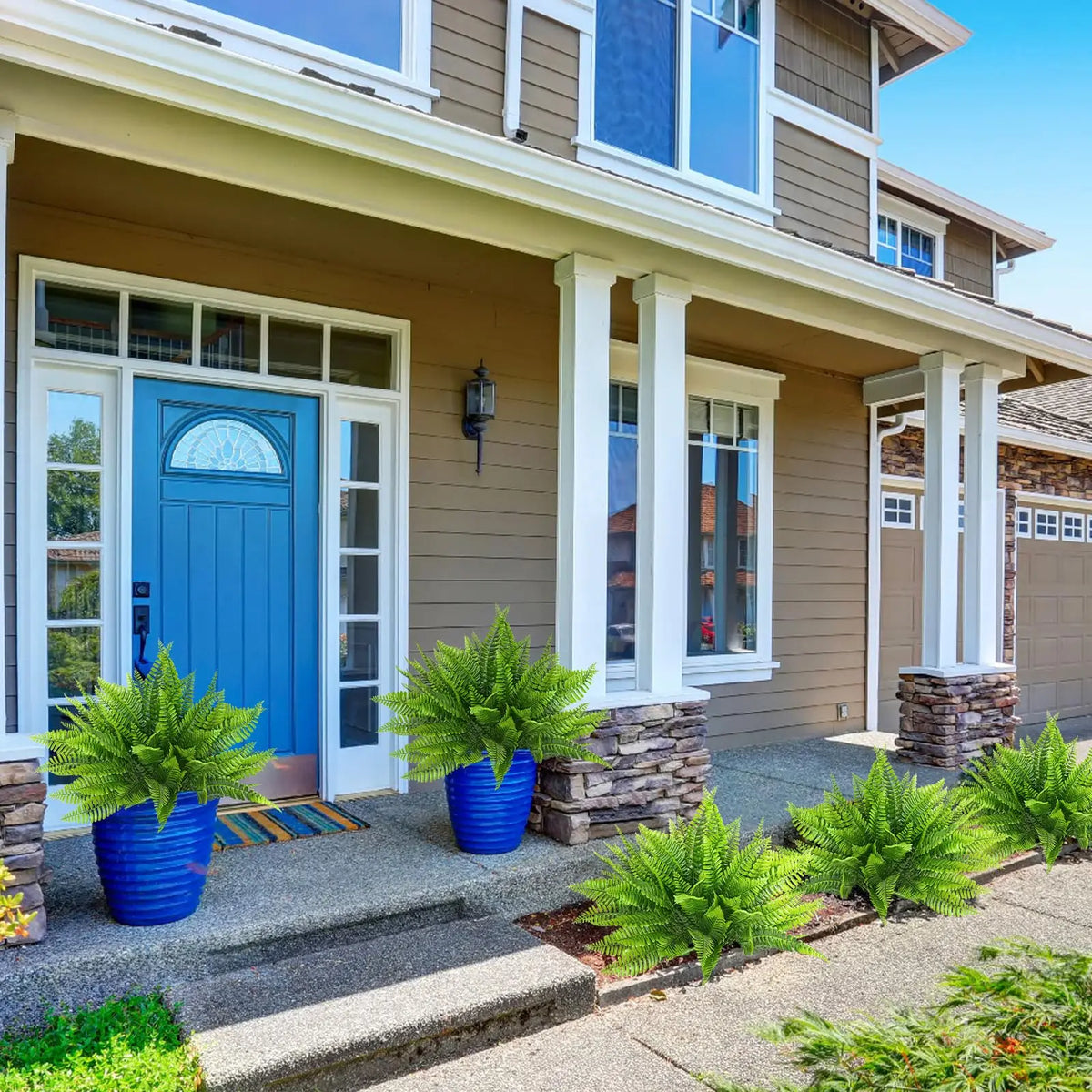 A row of vibrant blue artificial Boston ferns and shrubs planted in pots along the foundation of a house.