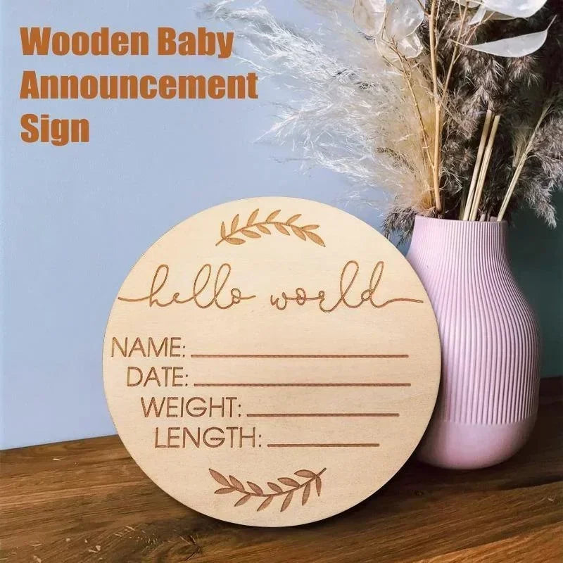 A round wooden baby announcement sign with the text hello world and lines for name date weight and length, displayed next to 