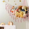 A multi-use storage hammock made of pink and white fabric hangs on a wall, filled with various stuffed toys.