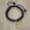 A black beaded bracelet with a gold charm featuring the zodiac symbol for Libra.