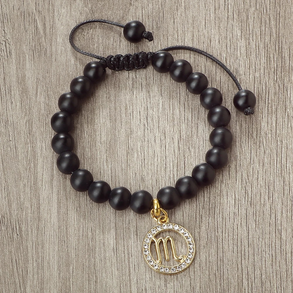 A black beaded bracelet with a gold charm featuring the zodiac symbol for Libra.