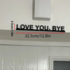Black metal wall art sculpture with the text LOVE YOU BYE mounted on a white wall.