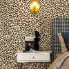 A close-up of a room decorated with retro leopard print wallpaper and a gold lamp above a nightstand.