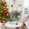 Artificial Norfolk Pine branches with red berry stems used for holiday decor on a white table.