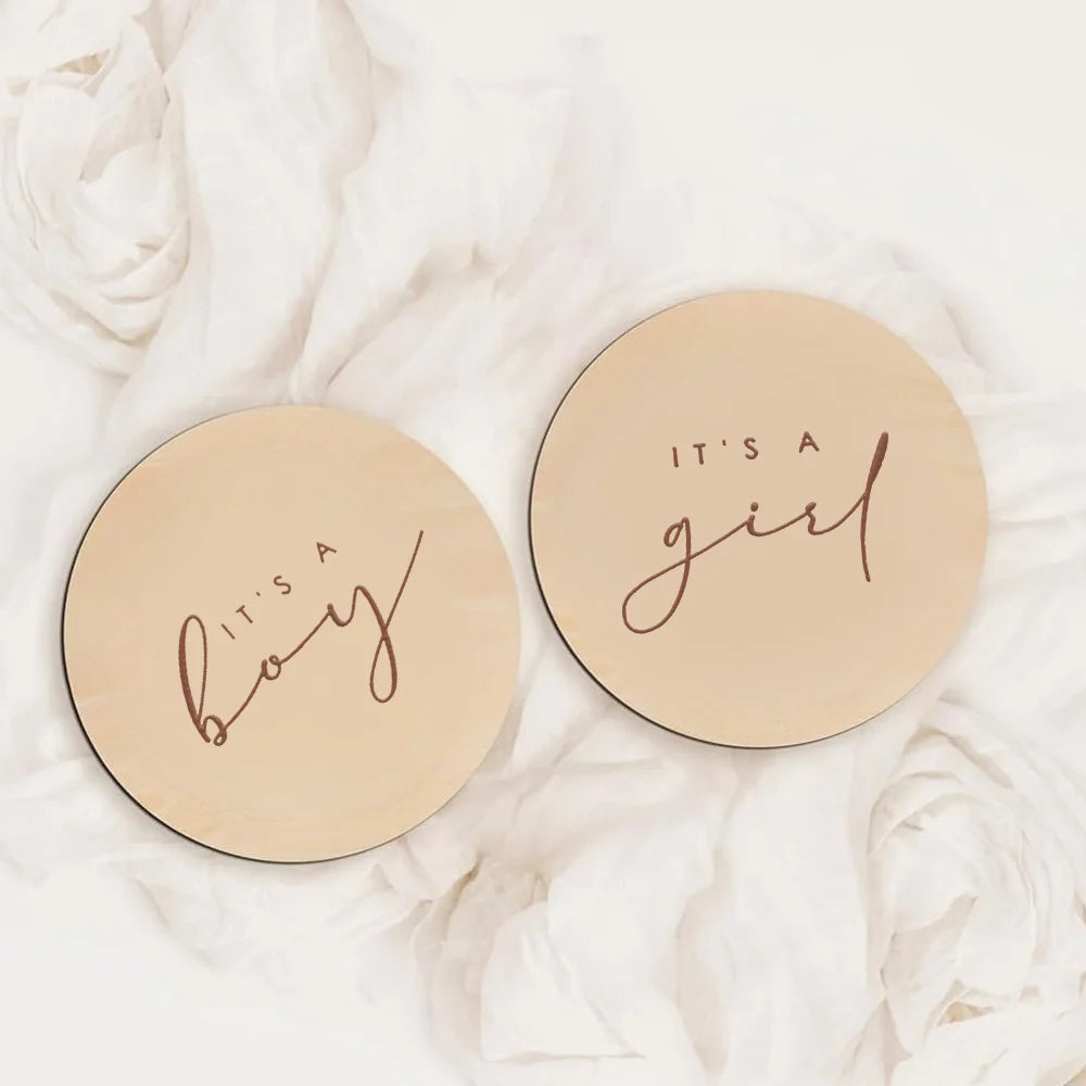 Two round wooden plaques, one labeled Boy and the other Girl, resting on white fabric.