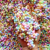 A hand holds a large quantity of pastel foam beads in various colors and shades for crafting.